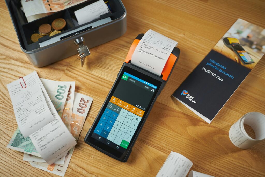 A modern payment terminal with receipts, cash, and manual on a wooden table.